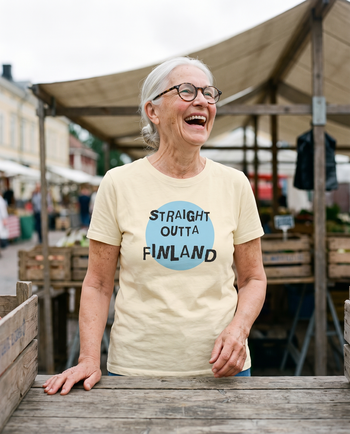 Straight Outta Finland t-shirt in soft cream, worn by Raija at a market table, Very Finnish Problems