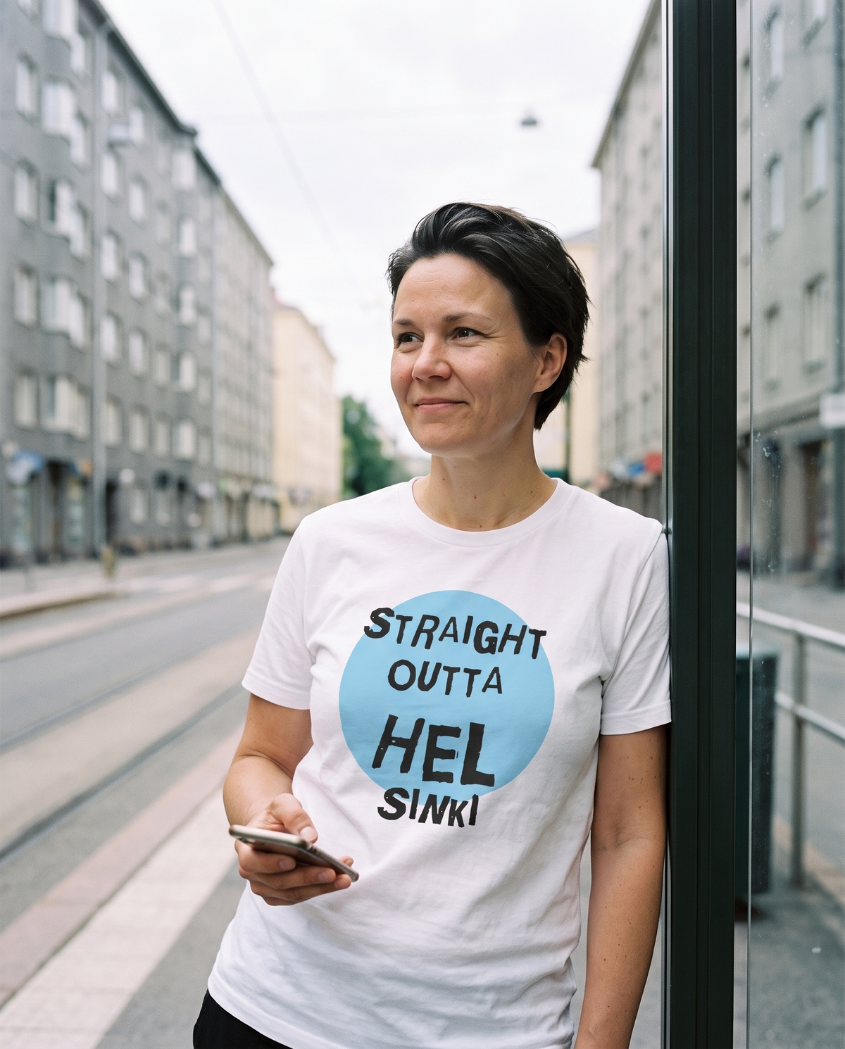 Straight Outta Hel II t-shirt in white, worn by Katja at a Helsinki tram shelter, Very Finnish Problems