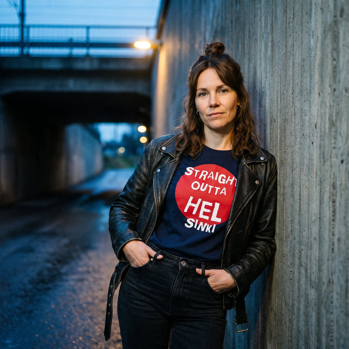 Straight Outta Hel t-shirt in navy with a red circle, worn by Suvi in a leather jacket in a Helsinki railway underpass at dusk, Very Finnish Problems