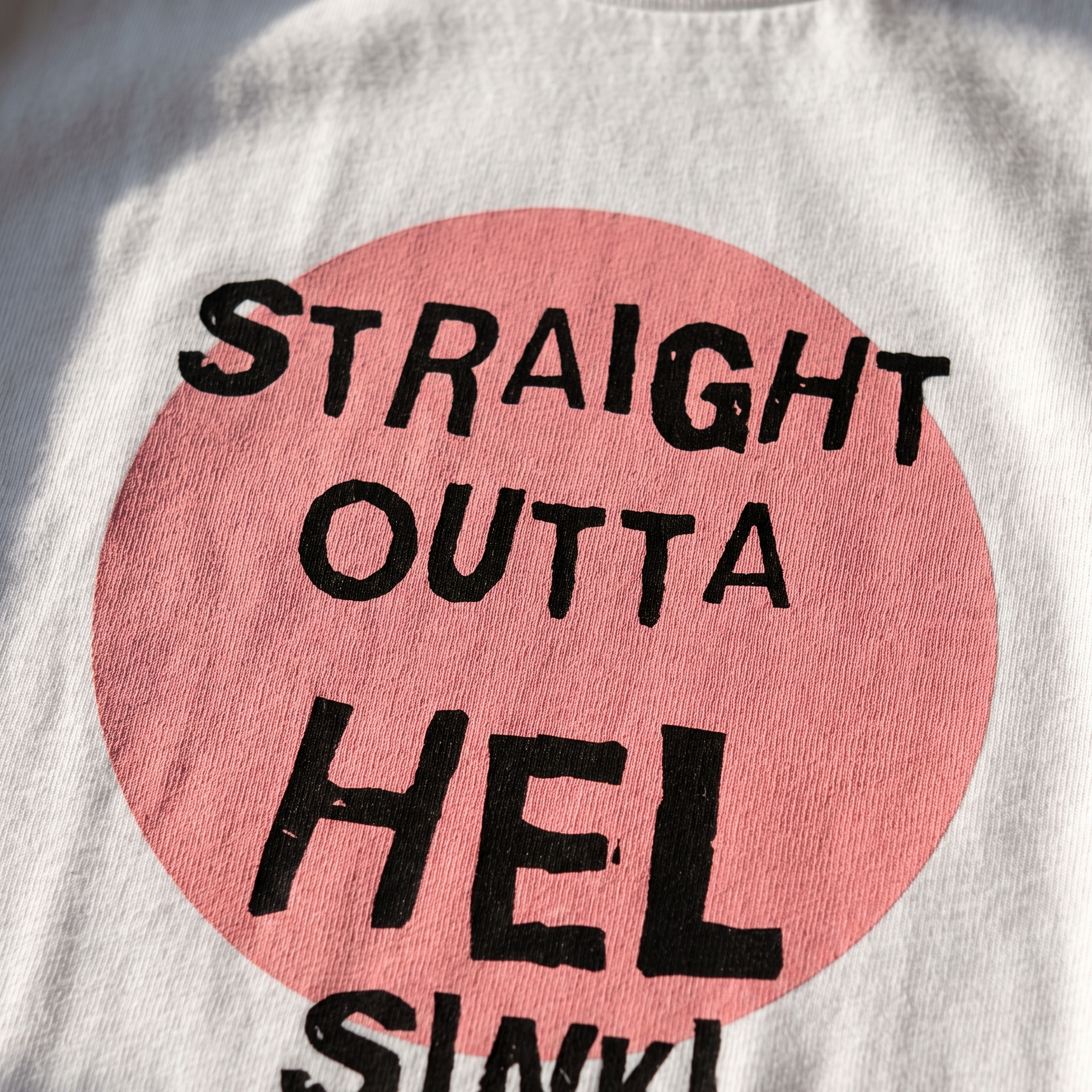 Close-up of the Straight Outta Hel print showing the pink circle and hand-lettered type on white cotton, Very Finnish Problems