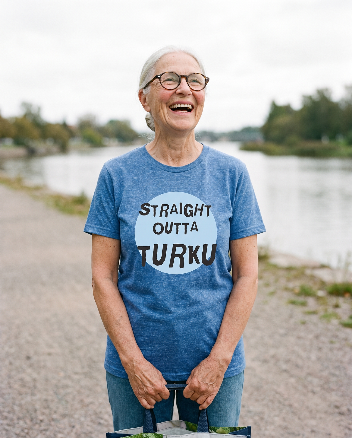Straight Outta Turku t-shirt in heather blue, worn by Raija on a riverside path, Very Finnish Problems