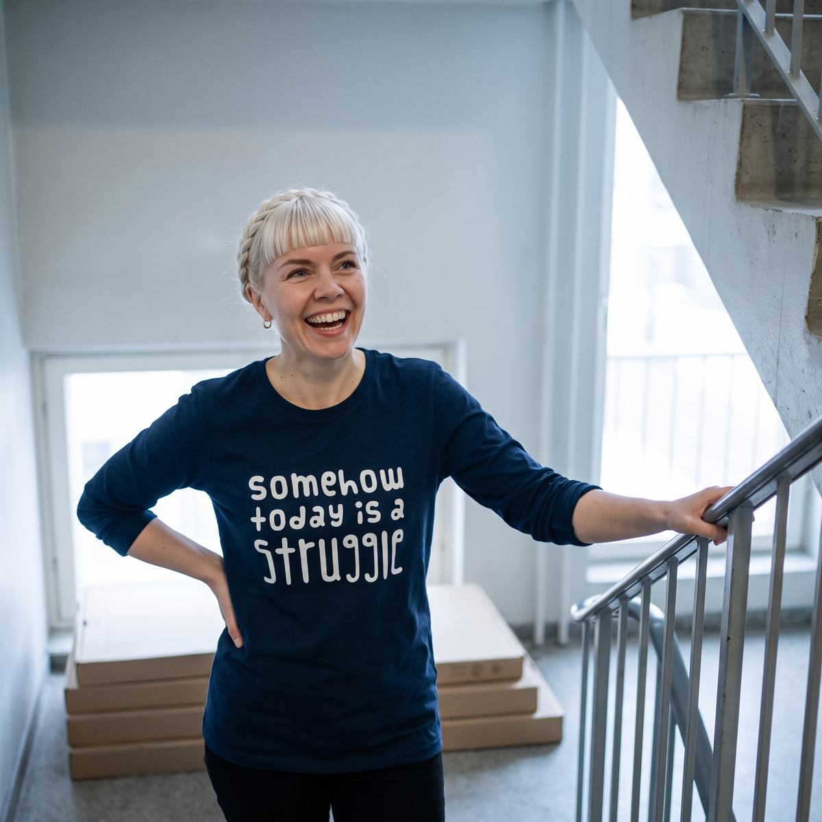 Somehow today is a struggle Finnish long sleeve tee in navy, worn by Venla laughing on a stairwell, Very Finnish Problems