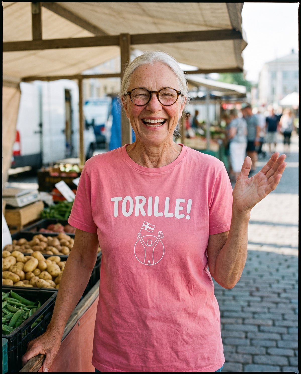 Torille t-shirt in charity pink, worn by Raija laughing at a Finnish market square stall, Very Finnish Problems