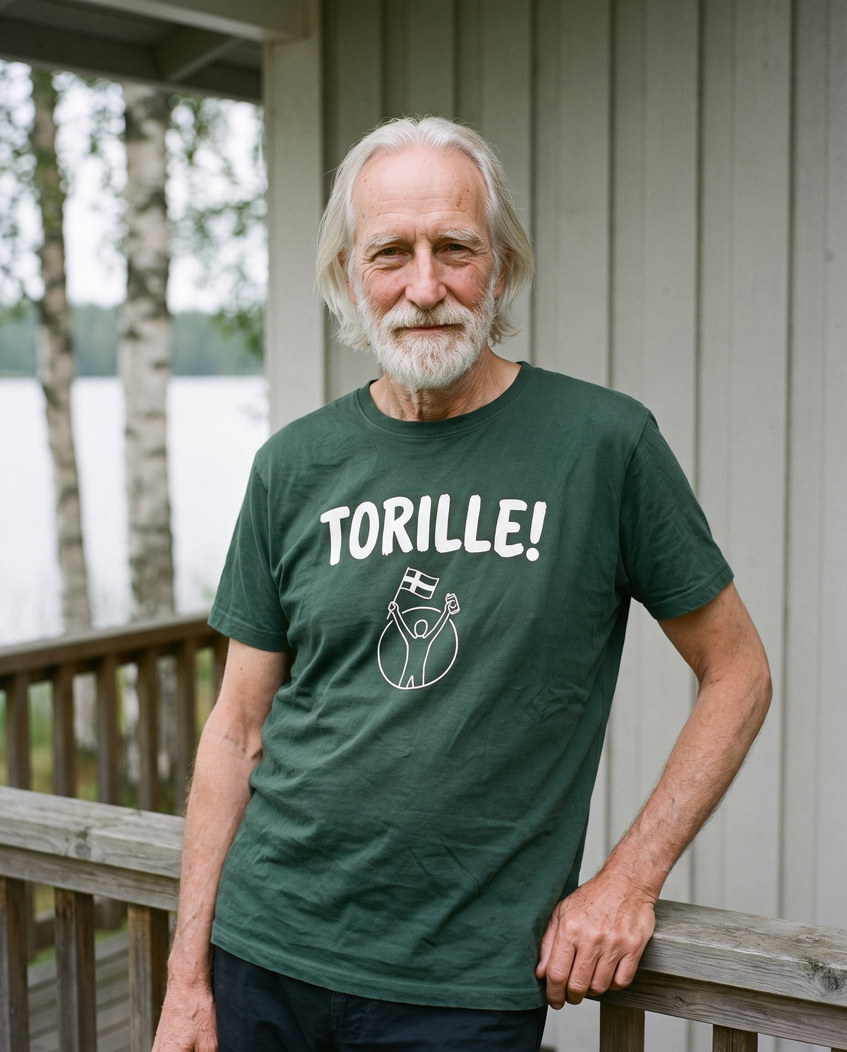 Torille t-shirt in forest green, worn by Pertti on a mokki veranda by a Finnish lake, Very Finnish Problems