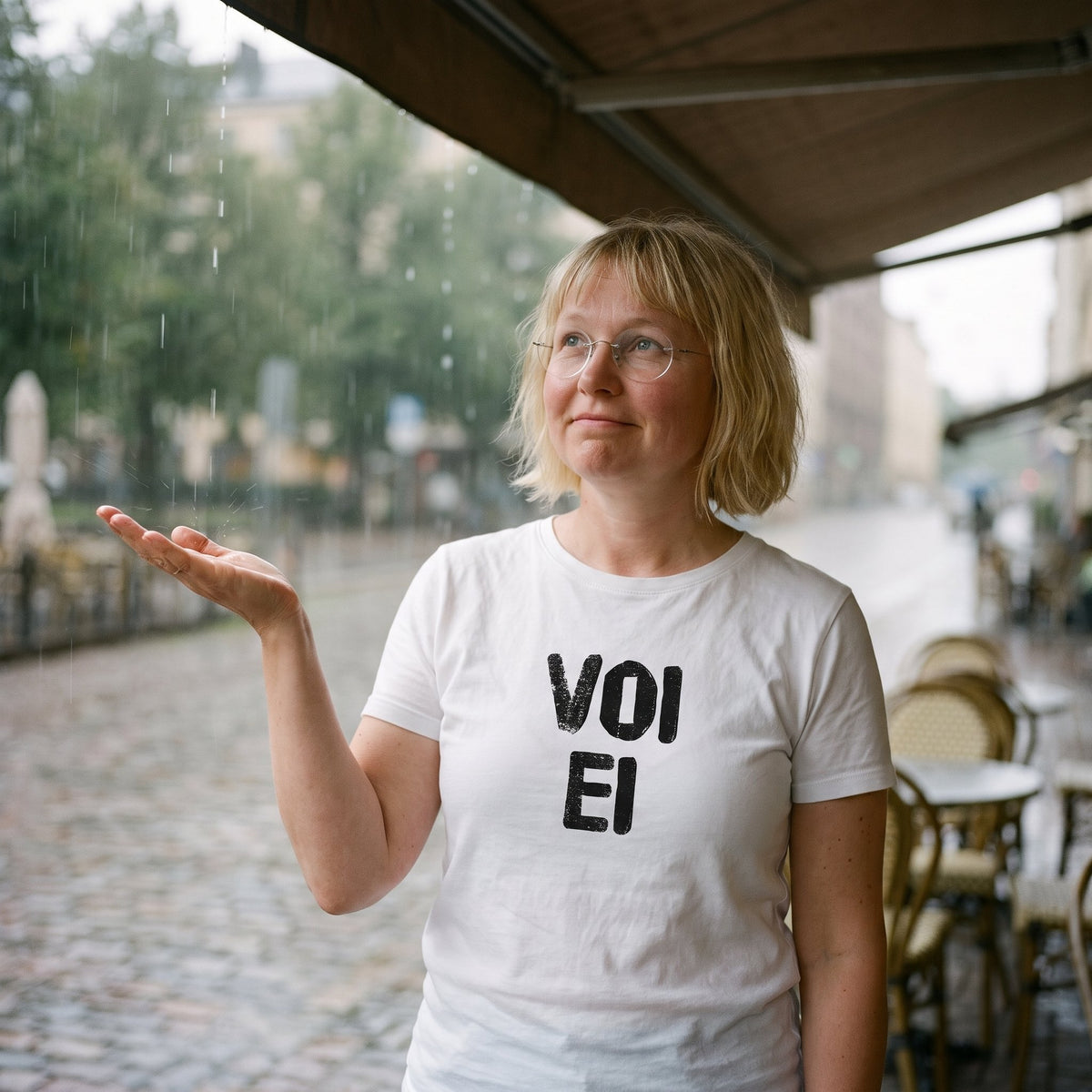 Voi ei Finnish language t-shirt in white, worn by Marika as rain starts at a café terrace, Very Finnish Problems