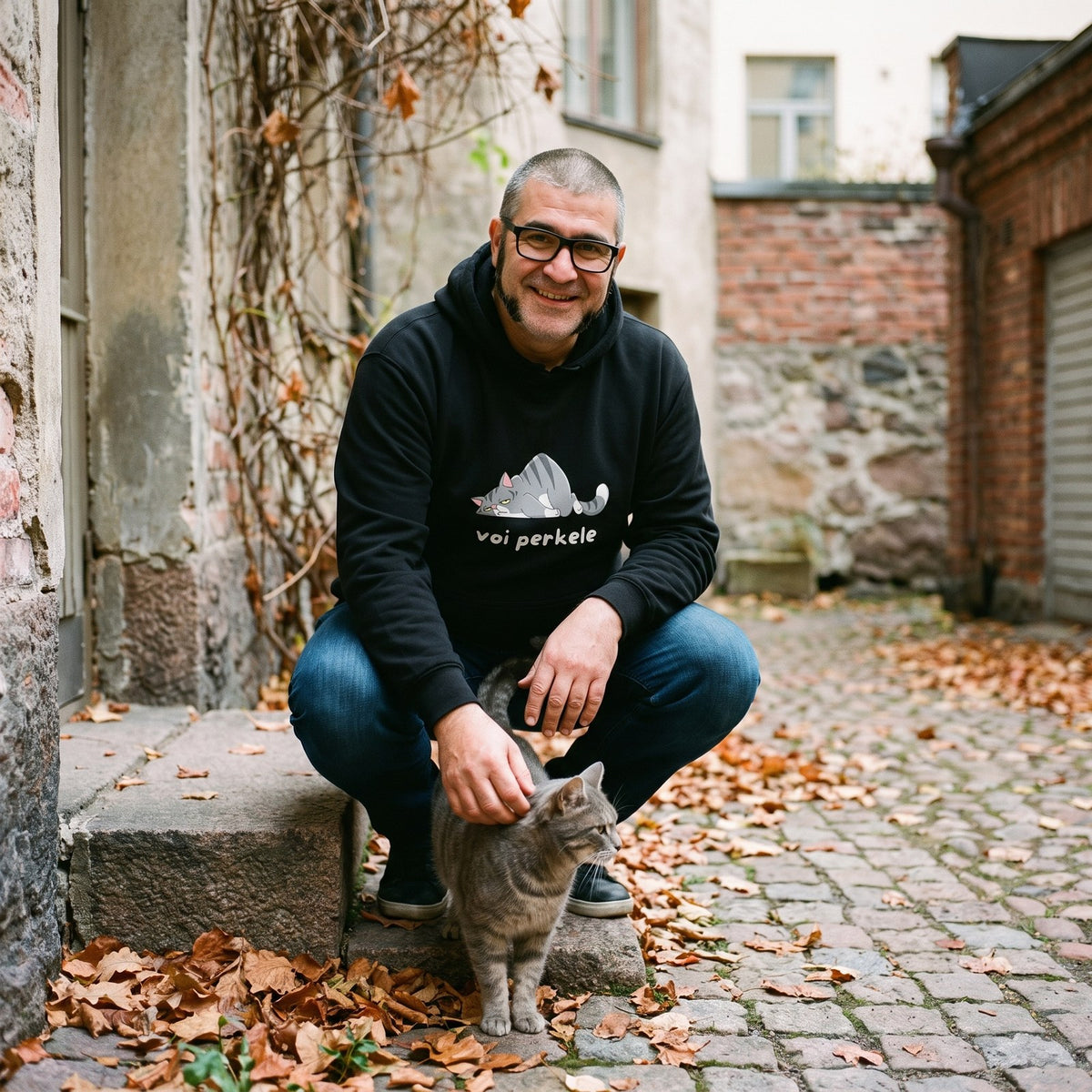Voi perkele hoodie in black, worn by Jaska crouching by a cat in a Helsinki courtyard, Very Finnish Problems