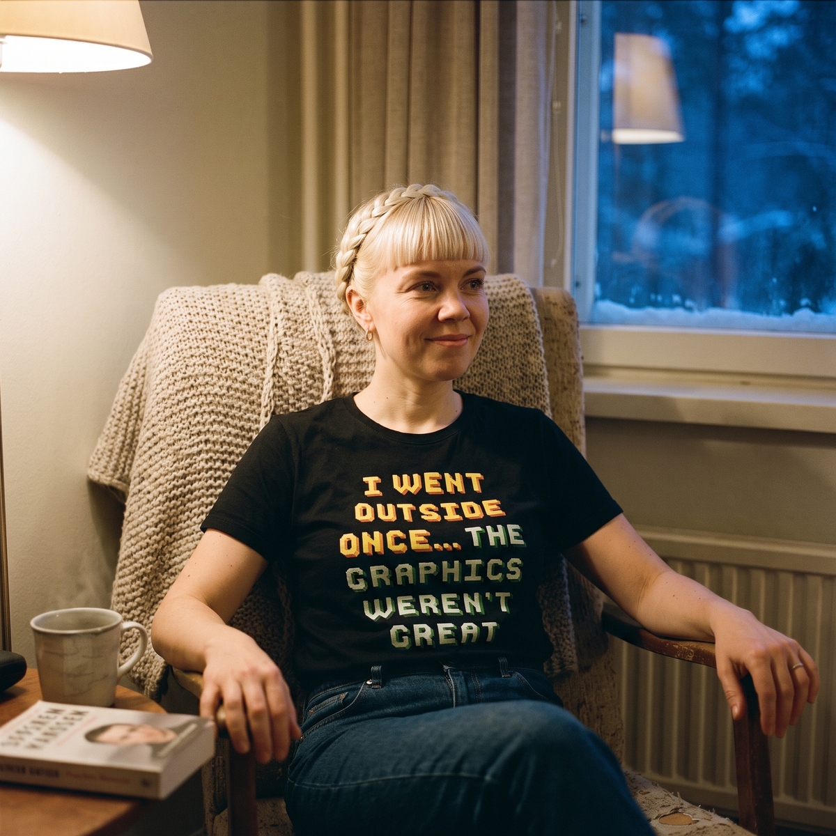 Went Outside Once t-shirt in black, worn by a woman in an armchair indoors on a snowy winter evening, Very Finnish Problems