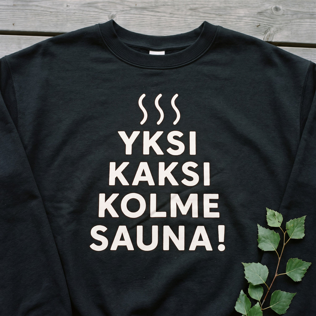 Close-up of the white Yksi, kaksi, kolme, sauna! print on a black crew neck sweatshirt, Very Finnish Problems