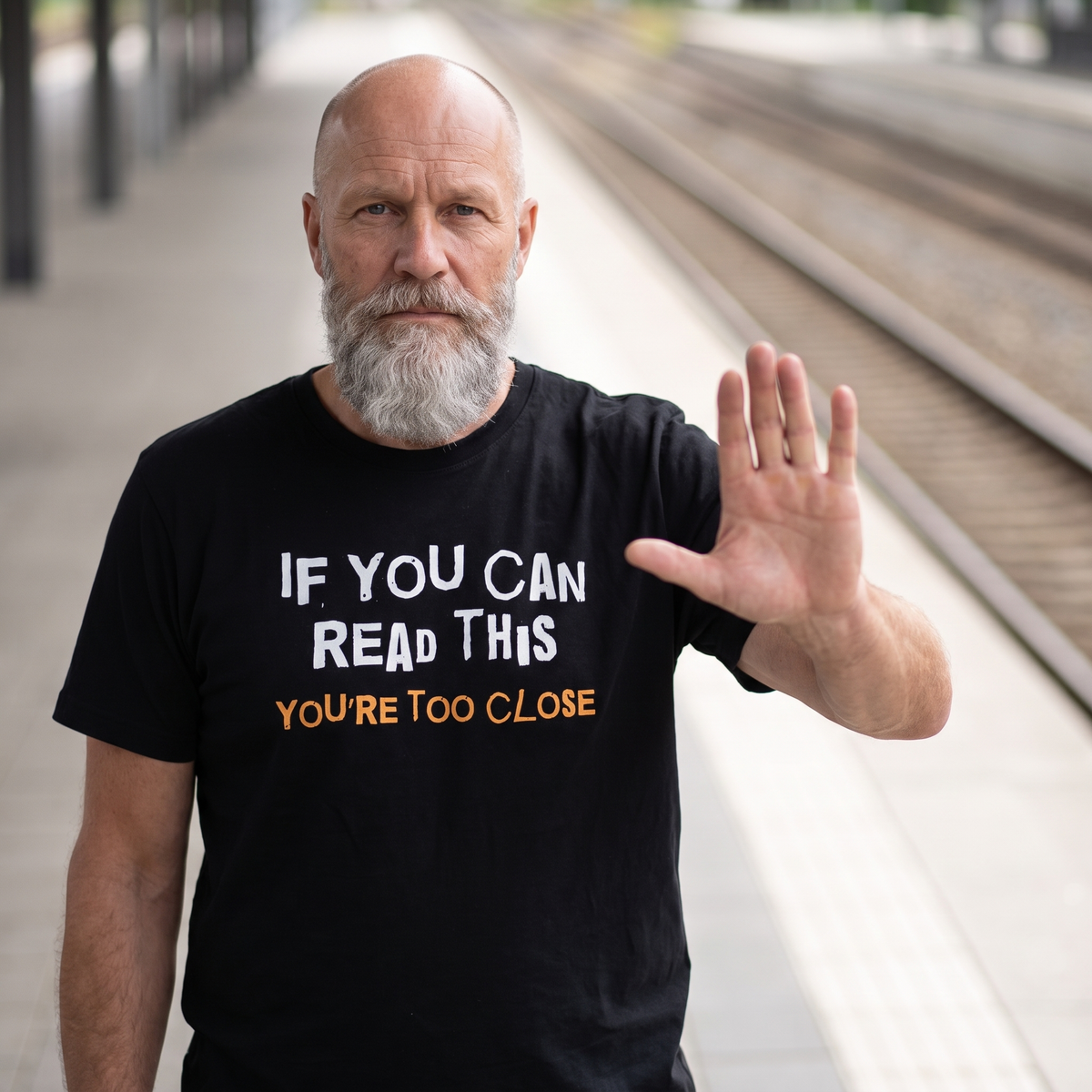 You're Too Close t-shirt in black, worn by Mikko holding up a hand on an empty platform, Very Finnish Problems